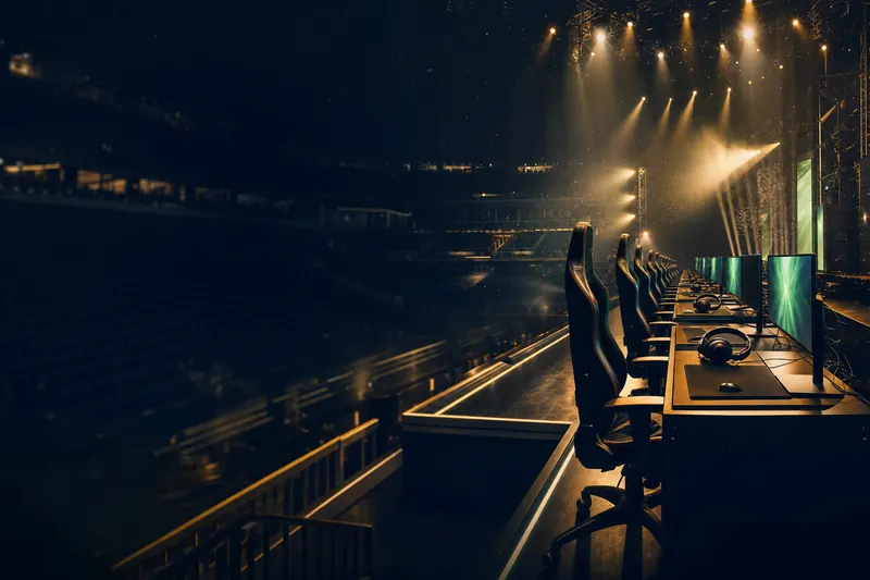 An empty esports arena with a row of gaming desks, glowing monitors and headsets under stage lights (AI-generated image)